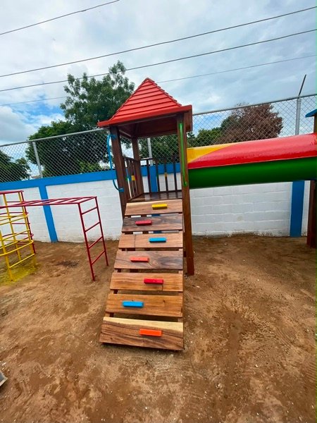 Parque infantil de madera con puente de cuerdas y techo rojo instalado por Ingeniarte